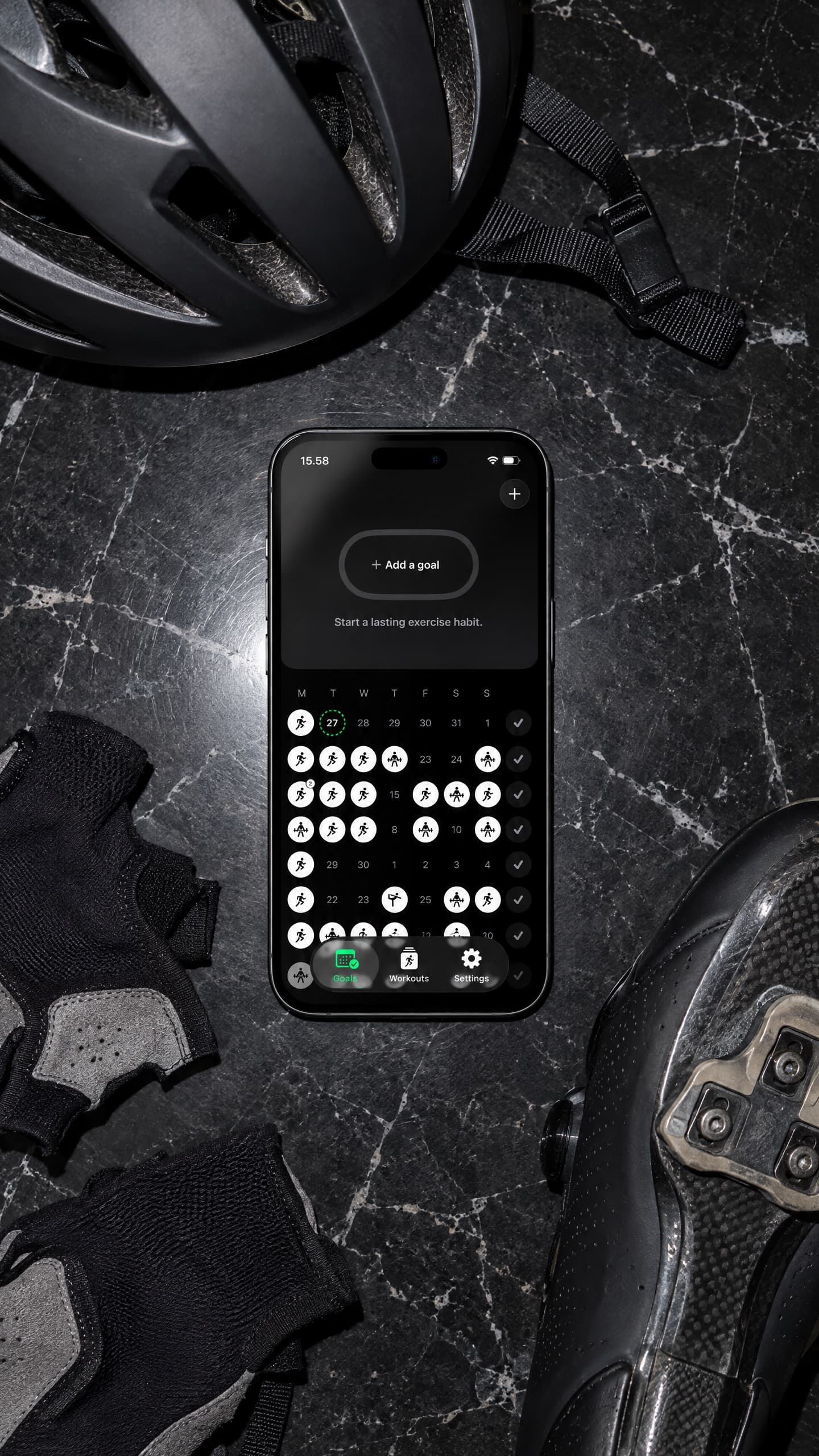 SweatCount on an iPhone, lying on dark stone among cycling kit: a helmet, gloves, a cycling shoe and a water bottle